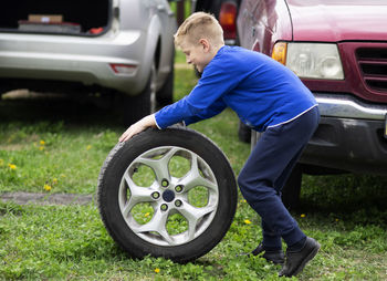 Side view full length of boy pushing tire on land