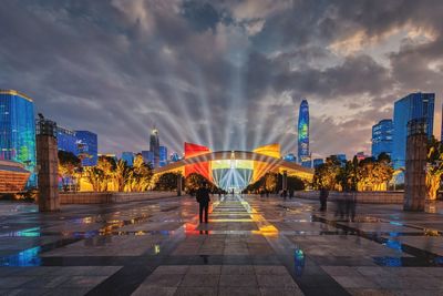 Illuminated footpath amidst buildings in city at dusk