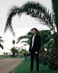 Young man standing against palm trees