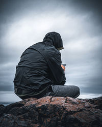 Man sitting on rock against sky