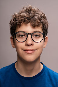 A cheerful teen boy with curly hair and eyeglasses, exuding confidence in a casual setting.