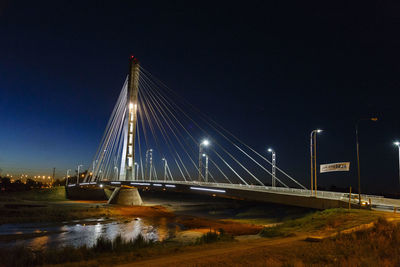 Illuminated bridge over river against sky at night