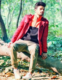 Full length of man sitting on log in forest