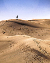 Man on sand dune in desert against clear sky