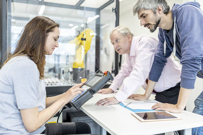 Colleagues watching woman programming robot arm with digital control