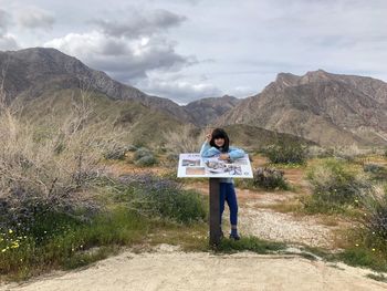 Full length of girl standing by information sign on land against mountains