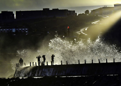 Silhouette people enjoying water splash on pier during sunset