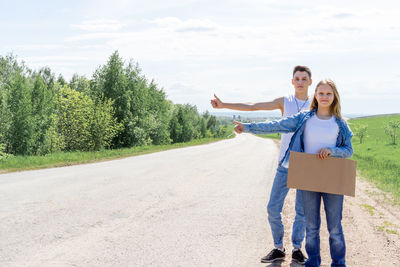 Portrait of young woman standing on road against sky