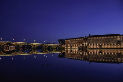 Arch bridge over river against clear blue sky at night