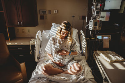 Pregnant woman touching stomach while sitting on bed in hospital