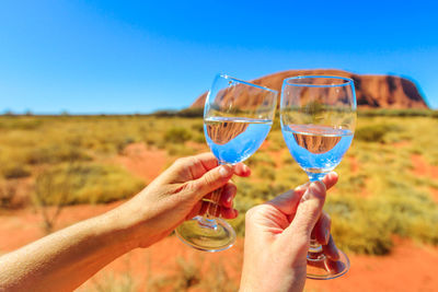 Close-up of hand holding drink glass against blue sky