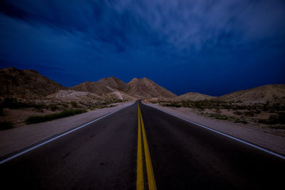 Road amidst landscape against sky at night leading to the mountains 