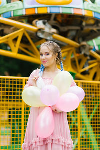 Beautiful caucasian young woman with balloons in amusement park in pink summer dress person