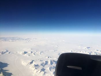 Airplane flying over snowcapped landscape against blue sky