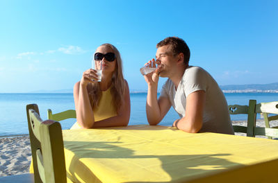 Couple drinking while sitting on beach