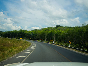 Empty road along trees and plants against sky
