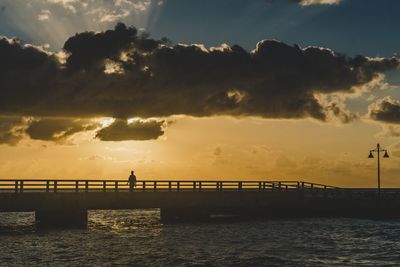 Silhouette bridge over sea against sky during sunset