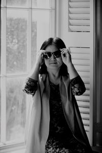 Portrait of woman wearing sunglasses while sitting against window
