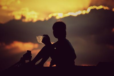 Silhouette girl sitting against cloudy sky during sunset
