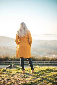 Rear view of woman standing on field against sky