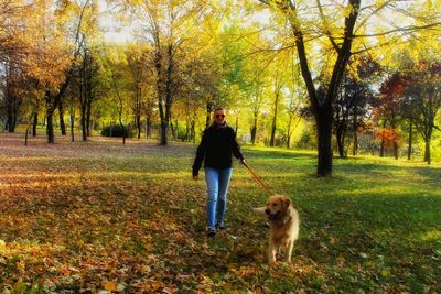 Woman with dog walking on field against trees