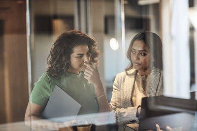 Businesswoman looking at laptop held by female colleague at office