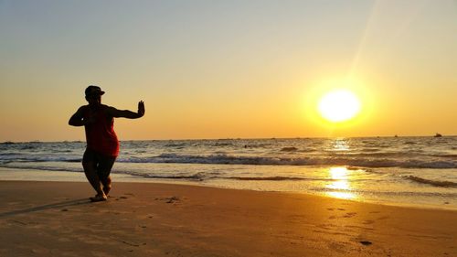 Full length of man performing martial arts on beach during sunset