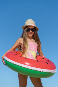 Portrait of a teenage girl in sunglasses and a hat with an inflatable ring against the sky. 