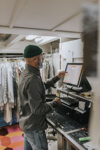 Side view of male tailor using computer while working in workshop