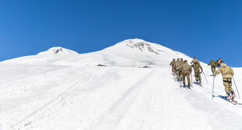 Group of people on snowcapped mountain against clear sky