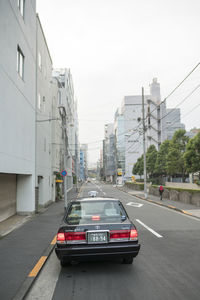 Cars on road by buildings against sky in city