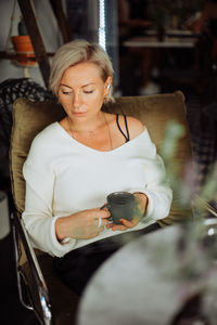 Thoughtful blond woman holding cup of tea while sitting in cafe