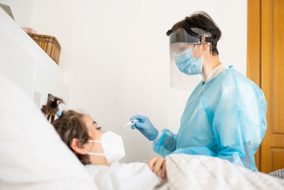 Doctor examining girl lying on bed at home