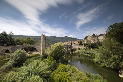 Arch bridge over river by buildings against sky