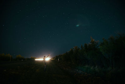 Man standing by illuminated trees against sky at night