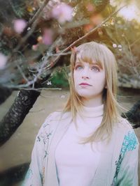 Beautiful young woman looking away standing by tree