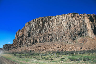 Low angle view of cliff against clear blue sky during sunny day