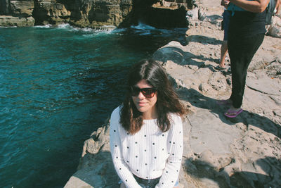 Young woman sitting by sea on rock