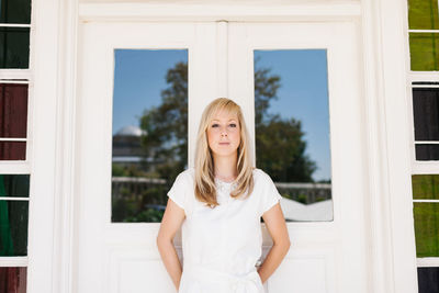 Portrait of a beautiful young woman standing against window