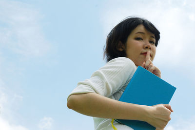 Low angle view of girl holding book against sky