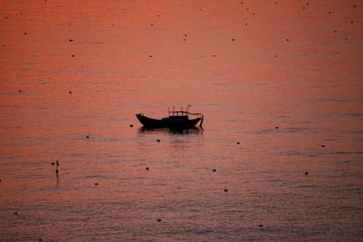 Boat sailing in sea against orange sky