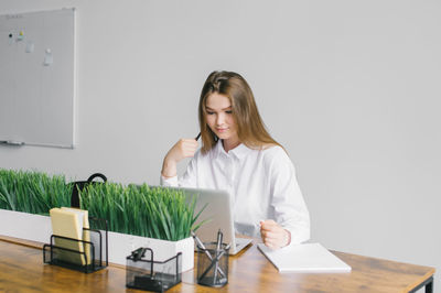 A cute girl is sitting at a wooden desk in the office working with a laptop and notepad