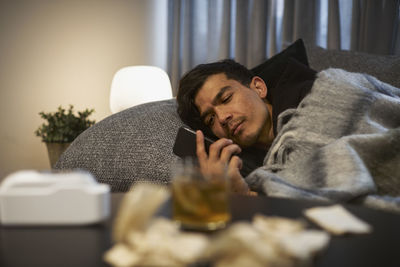 Young man lying on sofa and using smart phone