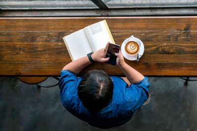 High angle view of man holding coffee while sitting on table