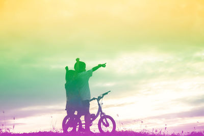 Man with bicycle against sky during sunset