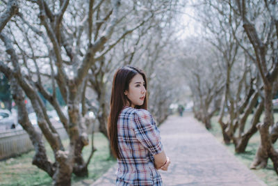 Young woman standing by bare trees in park