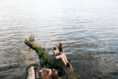 Rear view of woman sitting on rock by lake