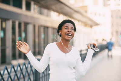 Portrait of a smiling young african woman listening to music with headphones outdoors on a city 
