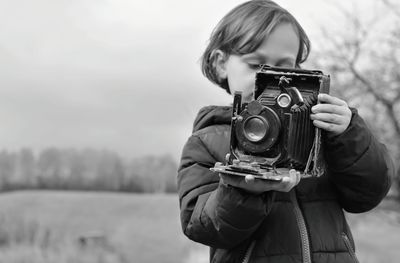Girl holding vintage camera against sky