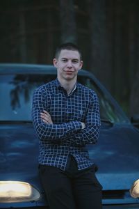 Portrait of man with arms crossed sitting on car hood